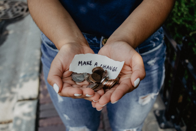 Open hands with some money and a note saying 'Make a change' 